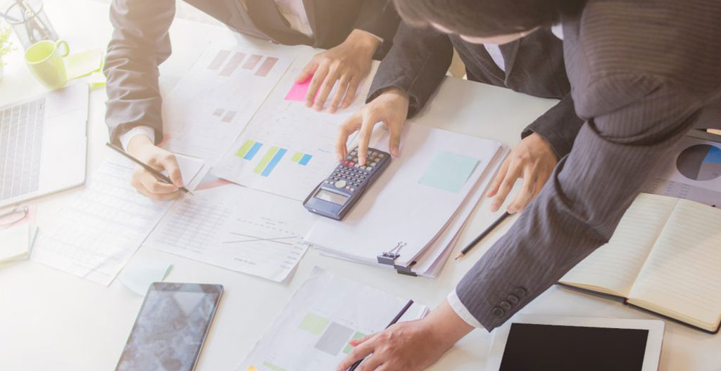 Gestionnaire d'entreprise analysant des documents contractuels et tableaux comparatifs de tarifs énergétiques sur un bureau professionnel moderne